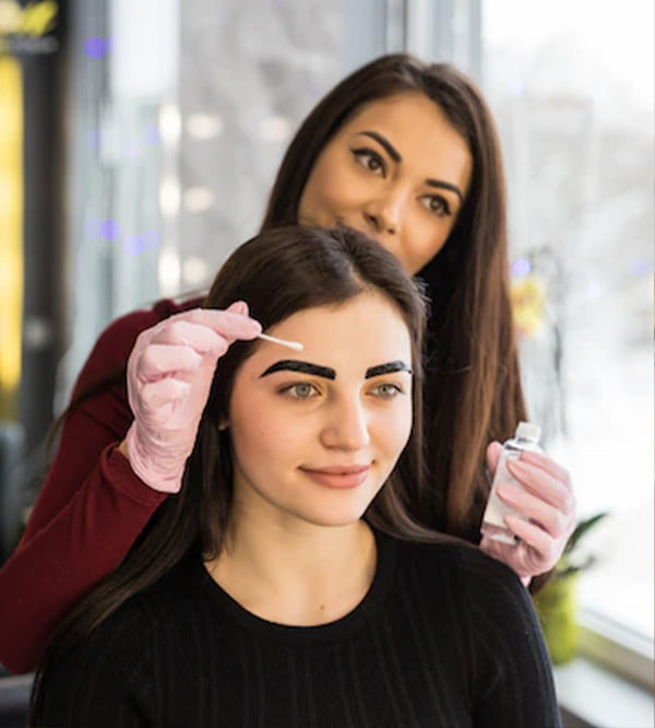 A woman receiving eyebrow treatment from another woman at a salon.