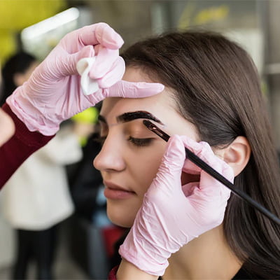 A woman receiving eyebrow treatment from a stylist.